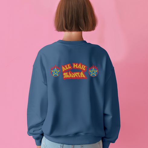 A Christmas sweatshirt featuring a playful design with a cartoon Baphomet goat character wearing a Santa hat. The design includes the text "All Hail Santa" above the goat, with pentagrams in flames on either side. The goat is depicted in a meditative pose, adding a humorous and irreverent twist to holiday attire.